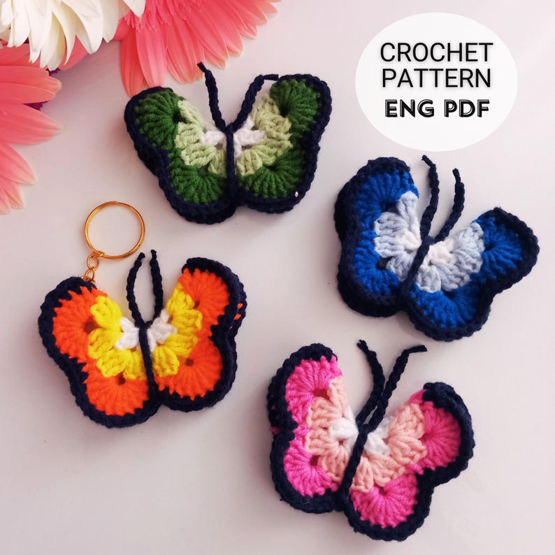 May include: A collection of colorful, crocheted butterfly decorations. One butterfly is attached to a gold keychain. The butterflies are in various colors, including orange, yellow, blue, green, and pink, with dark blue outlines. The text "CROCHET PATTERN ENG PDF" is in a white circle.