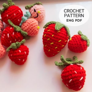 Puede incluir: Una colección de fresas hechas a mano con ganchillo en varios tamaños y tonos de rojo y rosa. Las fresas tienen copas verdes y detalles de semillas blancas. La imagen incluye el texto "CROCHET PATTERN ENG PDF".