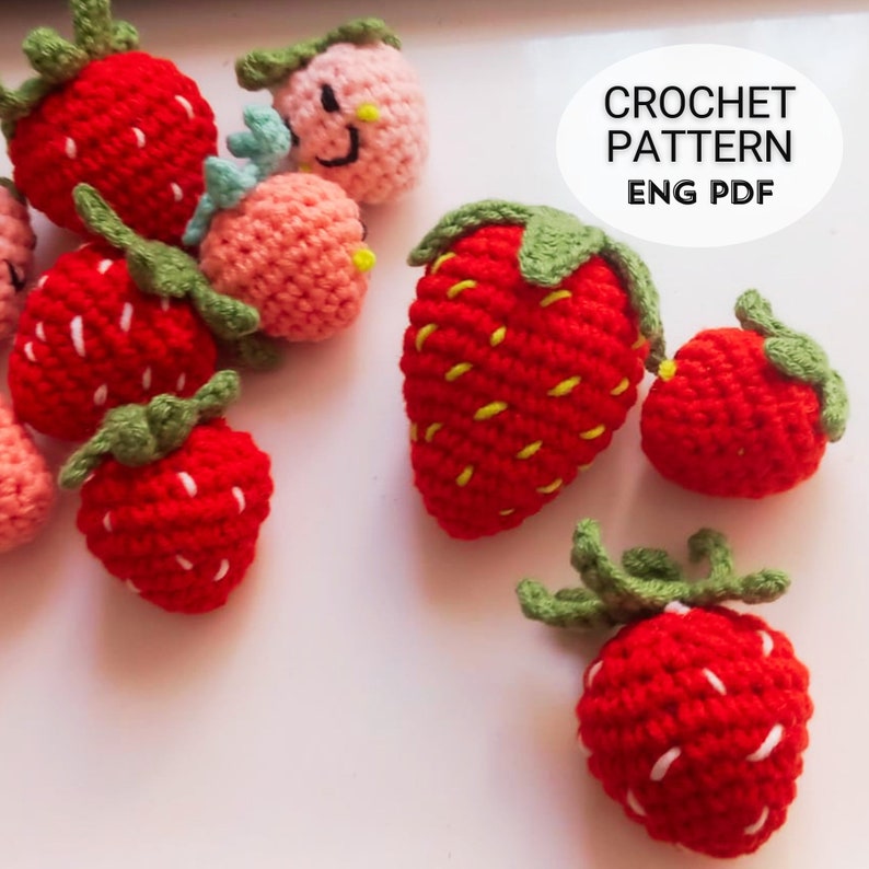 May include: A selection of handmade crochet strawberries in shades of red and pink. Each strawberry has a green leafy top and white seed detailing. The image includes the text "CROCHET PATTERN ENG PDF".