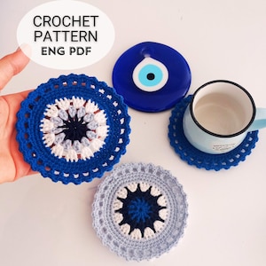 Könnte beinhalten: Drei gehäkelte Untersetzer mit einem blauen, weißen und grauen Augenmotiv. Die Untersetzer befinden sich auf einer weißen Oberfläche mit einem blauen Glas-Glücksbringer.