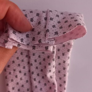 May include: Pink fabric with a small black floral pattern folded in half. The fabric is soft and has a smooth texture.