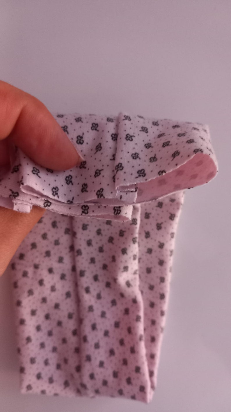 May include: Pink fabric with a small black floral pattern folded in half. The fabric is soft and has a smooth texture.