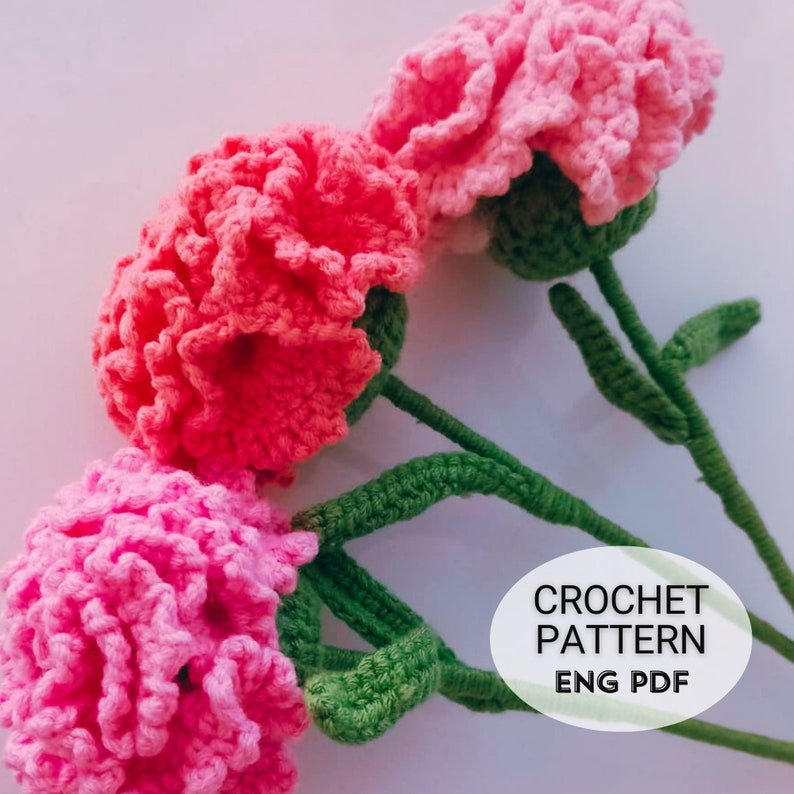 May include: Three pink crocheted carnations with green stems. The image includes the text "CROCHET PATTERN ENG PDF".