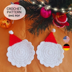 May include: Two circular white crochet coasters with scalloped edges, each topped with a red triangular hat featuring a white pom-pom. The text CROCHET PATTERN ENG PDF is visible in an oval overlay, alongside small US and German flag icons.