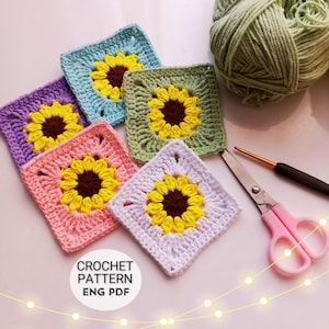 May include: Five square crochet motifs featuring a central brown and yellow sunflower design on light blue, purple, pink, sage green, and white backgrounds. A ball of sage green yarn, a crochet hook, and scissors are included. Text reads CROCHET PATTERN ENG PDF.