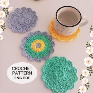 May include: Three crocheted coasters in different colors and patterns. One coaster is light blue, one is green with a yellow center, and one is green. The coasters are on a white surface. The text "CROCHET PATTERN ENG PDF" is visible in the image.