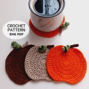May include: Crochet pattern for pumpkin-shaped coasters. The pattern is available in English and includes instructions for making three coasters in brown, beige, and orange.