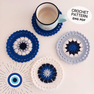 May include: Four crocheted coasters with a blue and white evil eye design. The coasters are round and have a white border. The evil eye design is in the center of each coaster. The coasters are on a white surface. CROCHET PATTERN ENG PDF