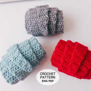 May include: Three crocheted items in gray, light blue, and red. The items are folded and stacked, showcasing a textured, handmade appearance. A white circle with the text "CROCHET PATTERN ENG PDF" is in the lower right corner.