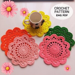 May include: A selection of brightly coloured, crocheted coasters in orange, pink, yellow, and green. A white mug with a cow design sits on a yellow coaster. The image includes the text "CROCHET PATTERN ENG PDF".