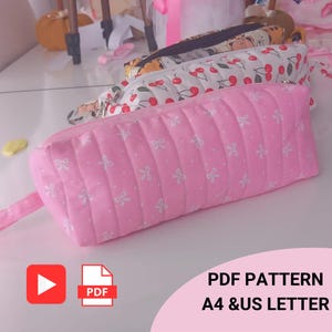May include: Pink quilted pencil case with white bow pattern. The pencil case has a zipper closure and a small fabric loop. Other pencil cases with cherry and animal patterns are visible in the background. The image includes the text "PDF PATTERN A4 & US LETTER".