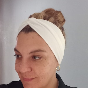 May include: A white turban headband with a twist detail. The headband is made of a soft, stretchy fabric and is perfect for keeping hair out of your face.