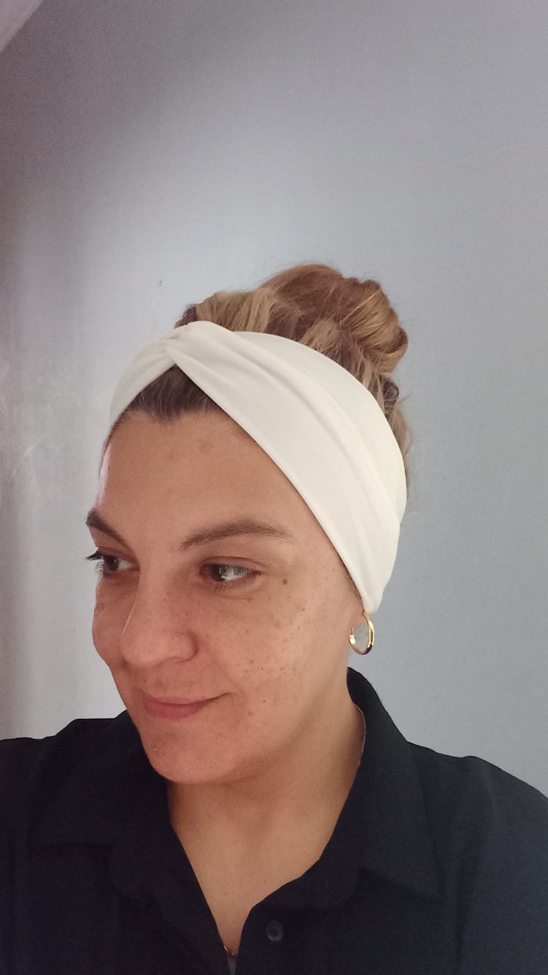 May include: A white turban headband with a twist detail. The headband is made of a soft, stretchy fabric and is perfect for keeping hair out of your face.