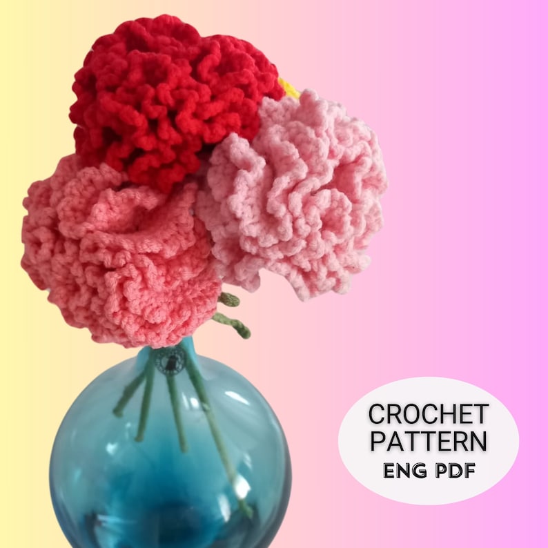 May include: A bouquet of crocheted carnations in shades of pink and red in a blue glass vase. The image includes the text "CROCHET PATTERN ENG PDF".