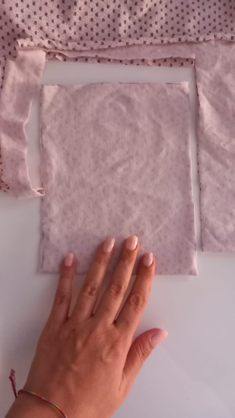 May include: A light pink fabric square with a slightly textured surface. The fabric is lying on a white surface.
