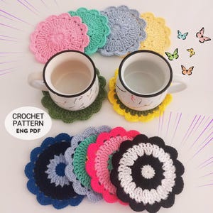 Puede incluir: Un conjunto de siete posavasos de ganchillo en varios colores, incluyendo rosa, verde, azul, amarillo, negro, blanco y gris. Los posavasos son redondos y tienen un borde festoneado. Los posavasos están dispuestos en un círculo alrededor de dos tazas.