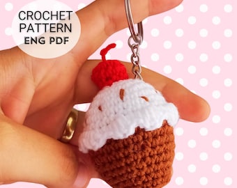May include: Crochet pattern for a cupcake keychain with a red cherry on top. The cupcake is brown with white frosting. The pattern is available in English PDF format.