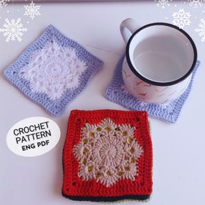 May include: Three crocheted coasters with different coloured borders and intricate designs in the centre. The coasters are made with white, light blue, red, and beige yarn. The text "CROCHET PATTERN ENG PDF" is visible in the image.