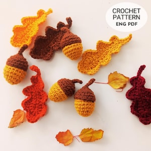 May include: Crocheted autumn-themed decorations, including acorns and leaves in shades of orange, yellow, and brown. The image includes the text "CROCHET PATTERN ENG PDF". These handmade items are perfect for fall crafting projects.
