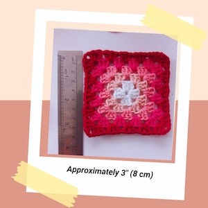 May include: A square, crocheted item in shades of red, pink, and white. The item is approximately 3 inches (8 cm) across. The text "Approximately 3" (8 cm)" is visible in the image.