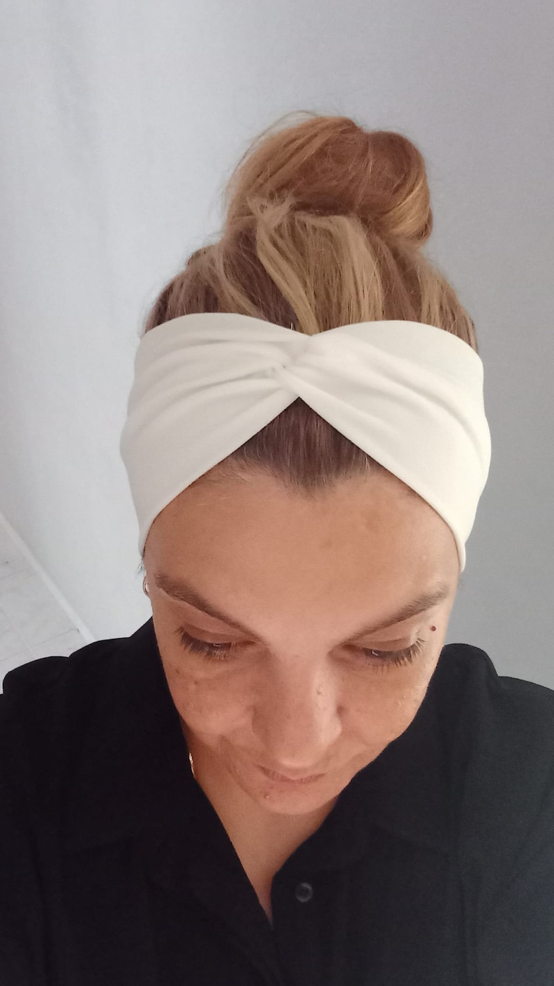 May include: A white turban headband with a twisted knot on top. The headband is made of a soft, stretchy fabric.