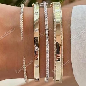 May include: A collection of gold and diamond bracelets. The bracelets vary in style, including a thin diamond tennis bracelet, a gold bangle with diamonds, and a wider gold bangle with a diamond border. The bracelets are displayed on a wrist.