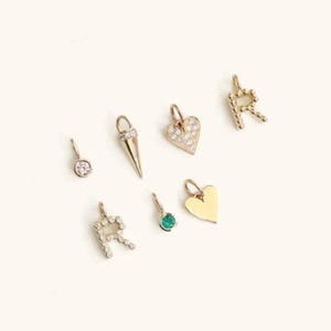 May include: A selection of gold-coloured charms, including a round charm with a single stone, a spike charm, two heart-shaped charms, and two letter "R" charms. One heart charm is encrusted with small stones, and one letter "R" charm is also encrusted with small stones.
