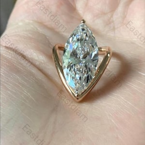 Könnte beinhalten: Ein roségoldener Ring mit einem großen, marquiseförmigen Edelstein. Der klare, facettierte Edelstein reflektiert das Licht. Der Ring hat ein einzigartiges, geometrisches Design.