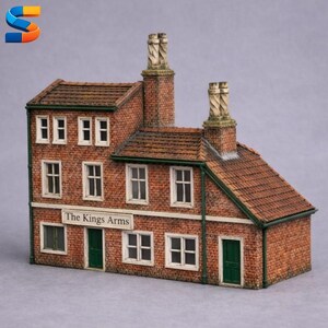 Può includere: Modello in miniatura dettagliato di un edificio in mattoni con tetto di tegole marroni, finestre con cornici bianche e porte verdi. L'insegna sopra la porta recita "The Kings Arms". Sono visibili due camini in mattoni.