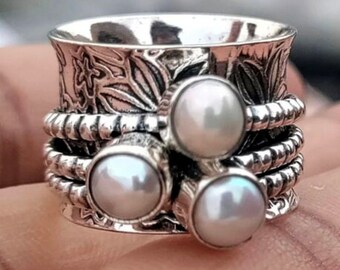 Könnte beinhalten: Ein silberner Drehring mit drei weißen Perlen. Der Ring hat ein strukturiertes Design und ist aus Sterlingsilber.