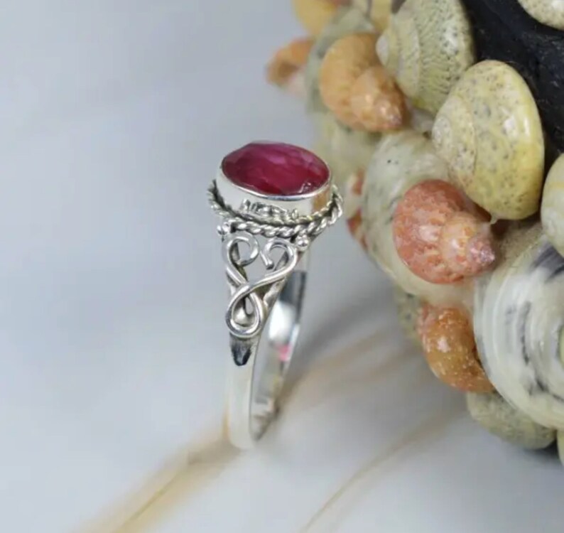 May include: A silver ring with a pink oval gemstone set in a twisted silver band. The ring has a delicate, ornate design.