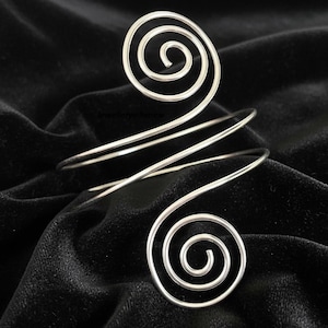 May include: A silver-toned arm cuff with a spiral design at each end. The cuff wraps around the arm with three parallel bands. The spirals are circular and the cuff is displayed on a black velvet surface.