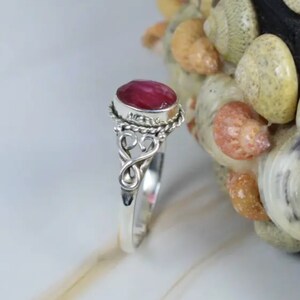 May include: A silver ring with a pink oval gemstone set in a twisted silver band. The ring has a delicate, ornate design.