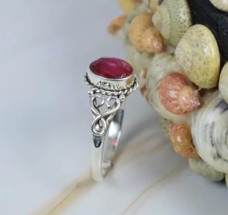May include: A silver ring with a pink oval gemstone set in a twisted silver band. The ring has a delicate, ornate design.