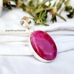 May include: A silver pendant with a large, oval-shaped, pink gemstone. The pendant is on a white surface.