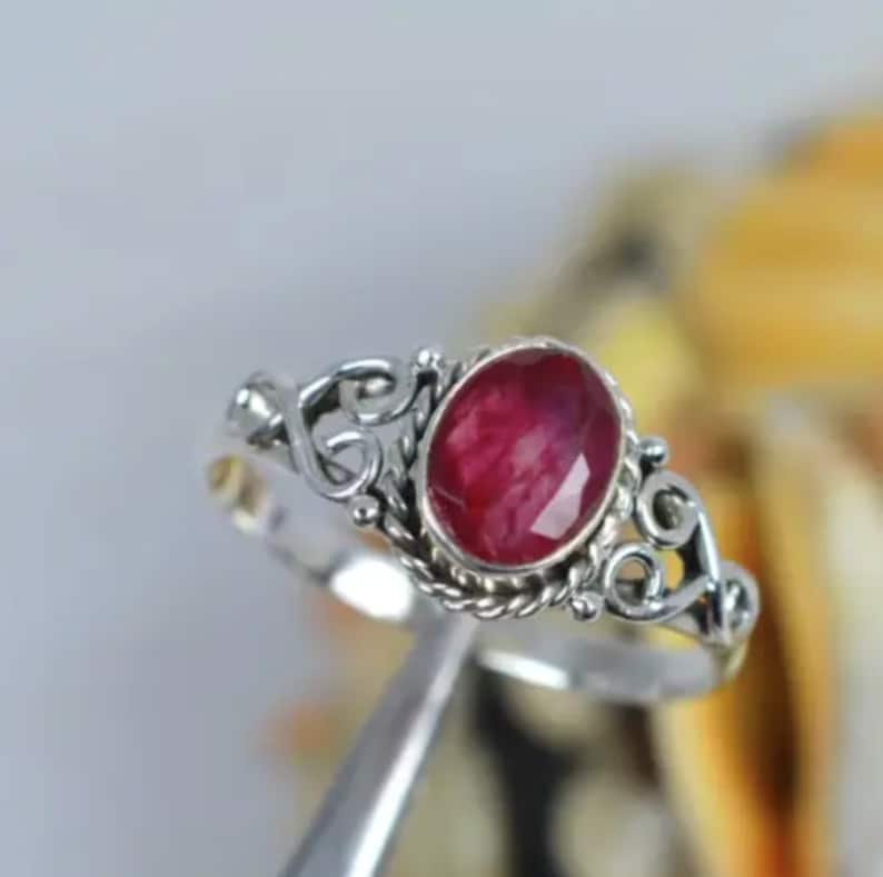 May include: A silver ring with a red ruby gemstone set in a delicate, ornate design.