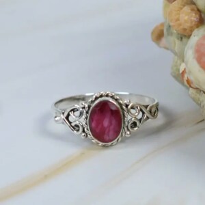 May include: A silver ring with a pink oval gemstone set in a delicate filigree design.