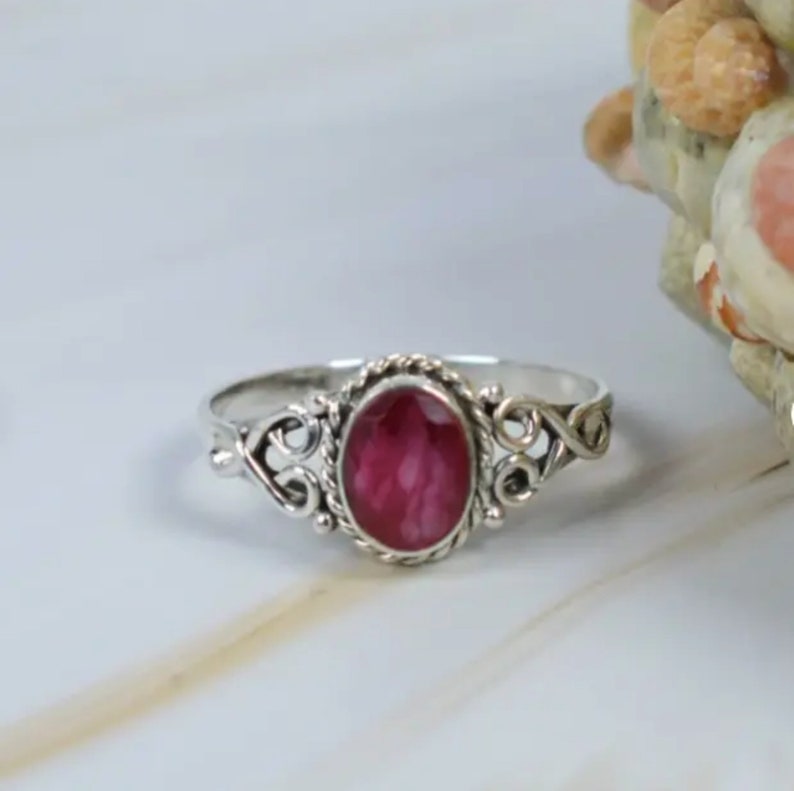 May include: A silver ring with a pink oval gemstone set in a delicate filigree design.
