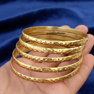 May include: A stack of six gold-colored bangles with a textured, hammered design. The bangles are stacked on top of each other, and the text "jewelleryvillanew" is visible on the top bangle.