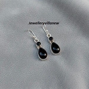 May include: Silver dangle earrings featuring black, teardrop-shaped stones. Each earring has a small, round stone above the larger teardrop. The text "Jewelleryvillanew" is visible.
