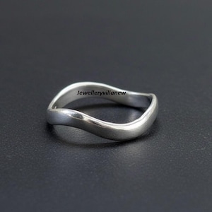 May include: A silver ring with a flowing, wavy design. The ring has a smooth, polished finish and a minimalist aesthetic. The text "Jewelleryvillanew" is visible on the ring.