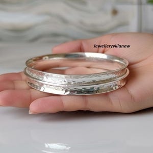 Puede incluir: Una pulsera de plata con textura martillada. La pulsera es redonda y tiene un diseño simple y elegante. La joya se sostiene en una mano.