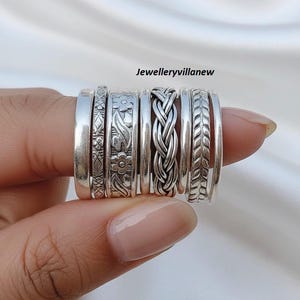 以下が含まれることがあります： さまざまなデザインのシルバーリングのコレクション。花柄、編み込み、幾何学模様などがあります。リングは一緒に表示され、さまざまなテクスチャとスタイルが示されています。リングは白い背景に対して保持されています。