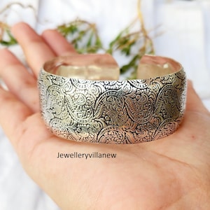 Puede incluir: Pulsera de brazalete de plata con un intrincado diseño floral.