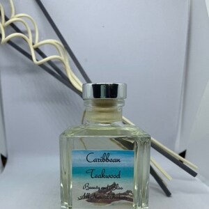 Peut inclure: Une bouteille en verre transparente avec un couvercle argent&eacute; et une &eacute;tiquette qui indique "Caribbean Teakwood Beauty and Bliss All Natural Perfumes". La bouteille est remplie d'un liquide clair et est entour&eacute;e de b&acirc;tonnets diffuseurs.