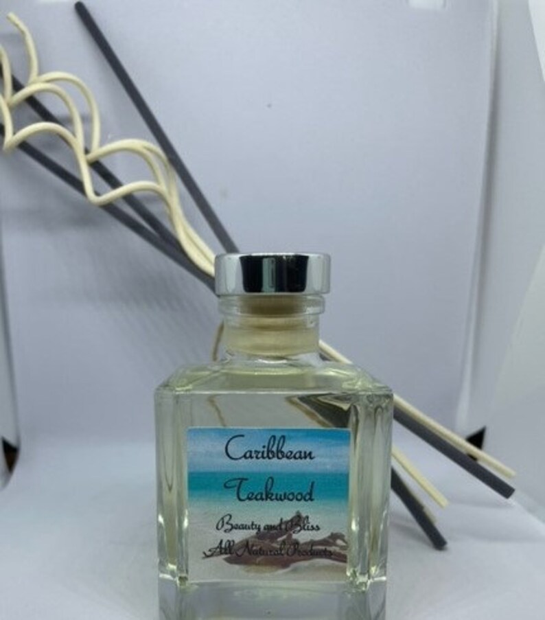 Peut inclure: Une bouteille en verre transparente avec un couvercle argent&eacute; et une &eacute;tiquette qui indique "Caribbean Teakwood Beauty and Bliss All Natural Perfumes". La bouteille est remplie d'un liquide clair et est entour&eacute;e de b&acirc;tonnets diffuseurs.