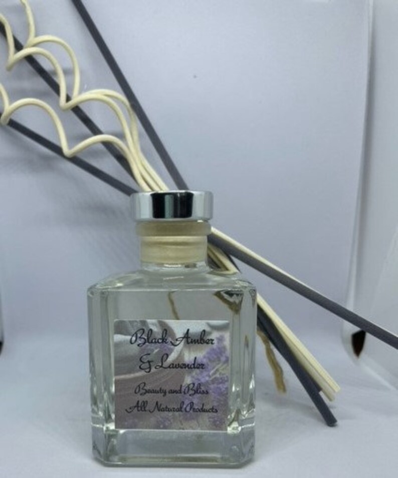 Peut inclure: Une bouteille en verre transparente avec un couvercle argent&eacute; et une &eacute;tiquette qui indique "Black Amber & Lavender" et "Beauty and Bliss All Natural Products". La bouteille est remplie d'un liquide clair et contient quelques b&acirc;tonnets.