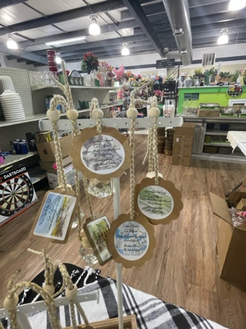 May include: A white metal stand with six brown paper tags hanging from it. Each tag has a different watercolour design and text. The tags are hanging from twine with wooden beads.