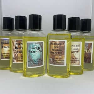May include: Six small glass bottles with amber liquid and black screw-top lids. Each bottle has a label with a different scent and name, including Mesme Beard, Fierce Bear Oil, Savage Beard Oil, Sandalwood and Bourbon Beard Oil, Tobacco and Bay Leaf Beard Oil, and Salty Mariner Beard Oil.