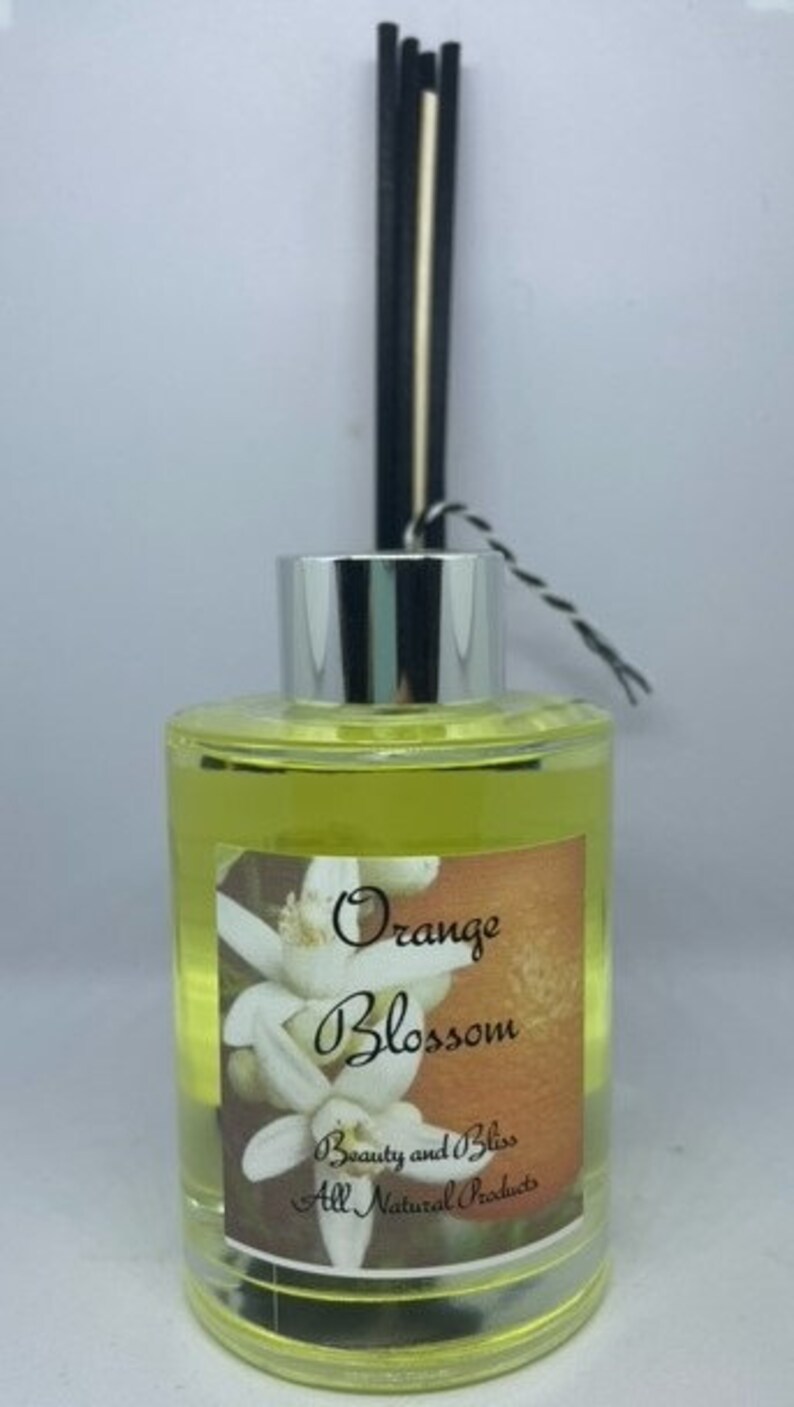 Peut inclure: Une bouteille en verre transparente avec un couvercle argent&eacute; et des roseaux noirs et blancs. La bouteille contient un liquide jaune et porte une &eacute;tiquette sur laquelle est &eacute;crit "Orange Blossom Beauty and Bliss All Natural Products".